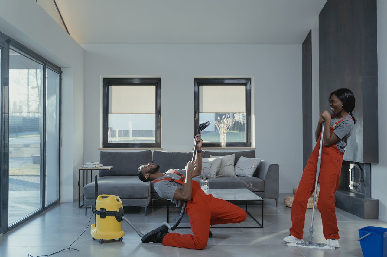 hero-img Fun and engaging cleaning session with a man and woman in overalls using cleaning tools in a modern living room.